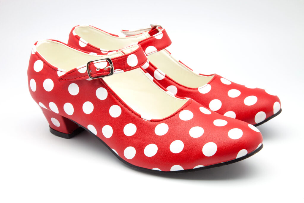 Red and white polka dot Mary Jane heels with buckle strap and low block heel, retro vintage style women’s shoes on a white background.