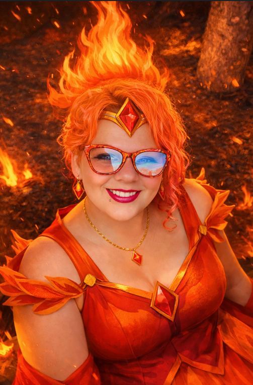 Woman dressed as a fiery fantasy character with flame headpiece standing in glowing fire background.