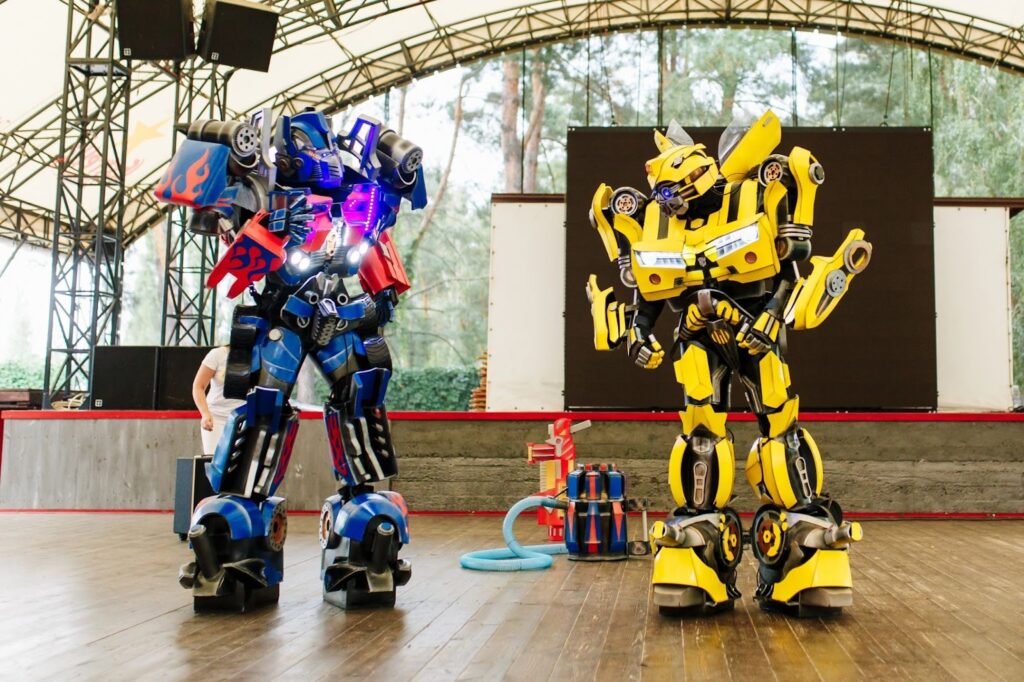 Two large Transformer robot costumes performing on stage, resembling Optimus Prime and Bumblebee.