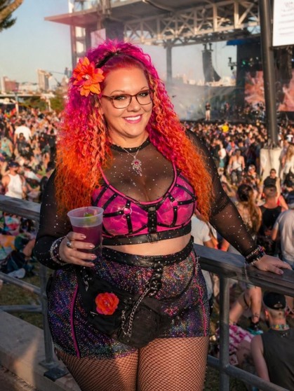 Woman in a sheer black sleeved netted top over a colorful outfit at an outdoor music festival