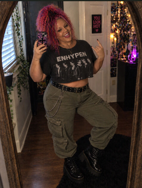 Woman posing in front of a mirror in a band tee and cargo pants.