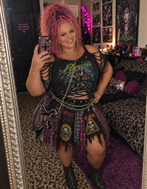 Woman posing in front of a mirror in a deconstructed band tee outfit and fishnets.