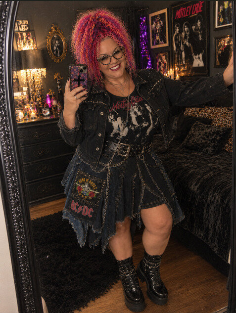 Woman posing in front of a mirror in a denim and patchwork band tee outfit.