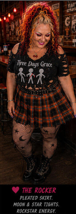Woman in plaid skirt and band tee modeling in a bar setting.
