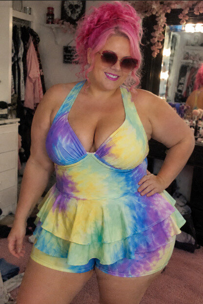 Woman in tie dyed two piece swimsuit posing for picture in sunglasses.